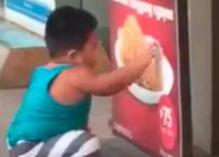 بالفيديو| طفل جائع يحاول تناول الدجاج من ملصق إعلاني