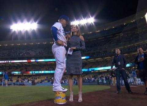 في لقطة طريفة.. لاعب بيسبول يقف على quotجردلquot ليحازي طول مذيعة