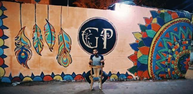 «كريم» مع إحدى رسوماته على الجدران