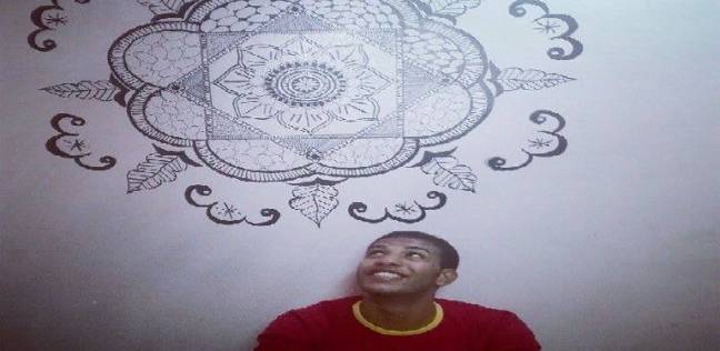 «أحمد» يجلس أمام حائط رسمه بمنزله