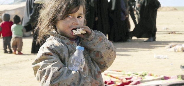 طفلة سورية تقضم قطعة خبز فى مشهد فرار عائلات سورية من مناطق القتال فى «باغوز» «أ.ف.ب»