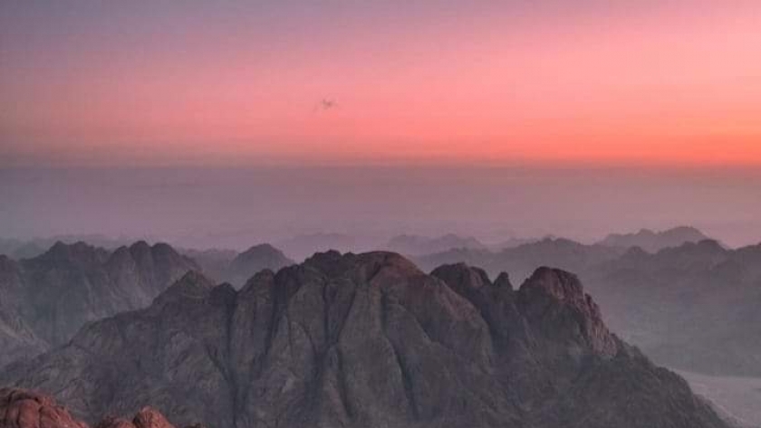 أحد السياح يشاهد شروق الشمس من فوق قمة جبل موسى