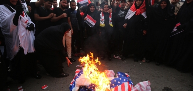 عراقيون يحرقون العلم الأمريكى فى بغداد احتجاجاً على الغارات الجوية الغربية على سوريا «أ.ف.ب»