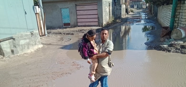 أحد أهالى قرية «الربع» بكفر الشيخ يحمل طفلته إلى المدرسة بسبب غرق الشوارع بمياه الأمطار