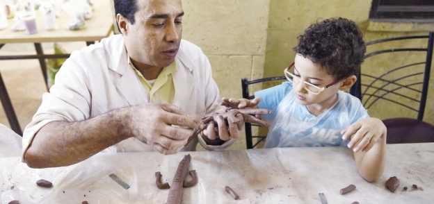 «مجدى» يعلم طفلاً فن النحت على الخذف