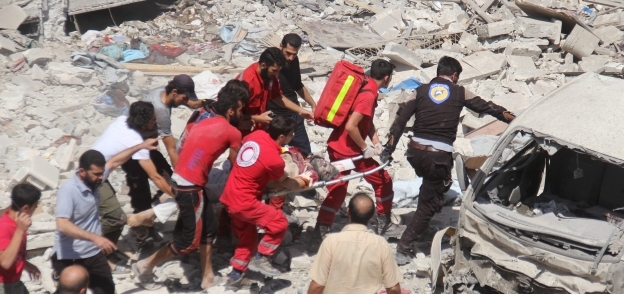 رجال الحماية المدنية ينتشلون إحدى الجثث بين أنقاض مبان سورية تحطمت فى الغارات «أ.ف.ب»