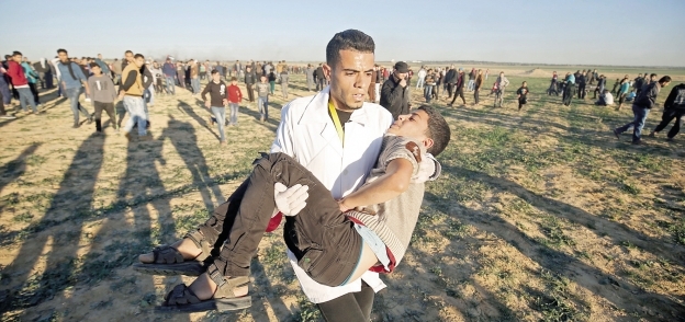 مسعف يحمل شاباً فلسطينياً بعد إصابته فى مسيرات العودة «أ. ف. ب»
