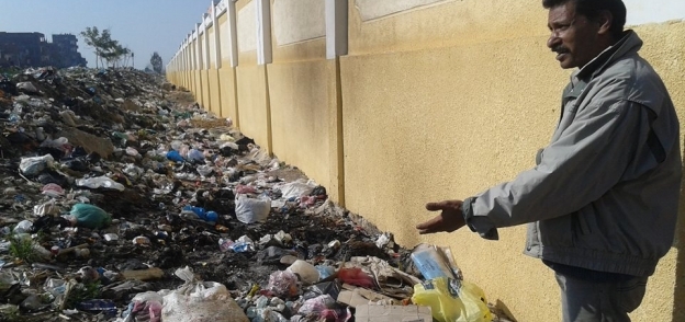 أحد المواطنين يشير إلى أكوام القمامة بجوار سور السكة الحديد