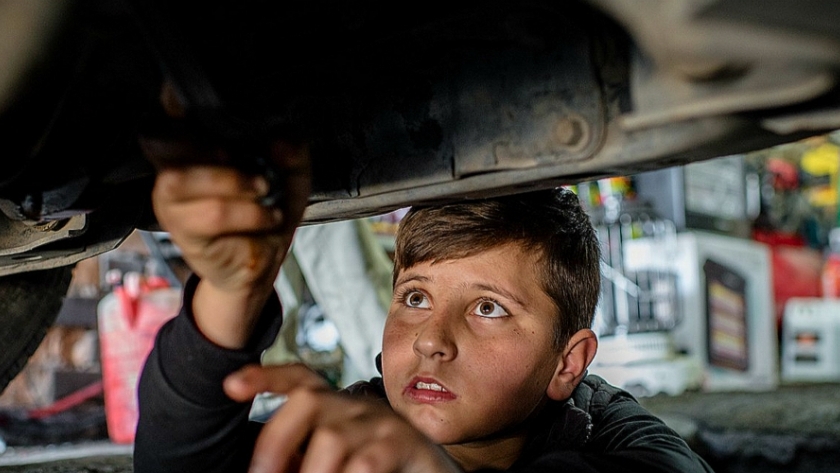 صورة من اليونيسف للاجئ سوري من حلب يعمل تحت سيارة في ورشة لإصلاح السيارات في العراق