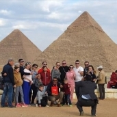 مجموعة ضمن فوج سياحي يلتقطون صورة تذكارية في منطقة الأهرامات